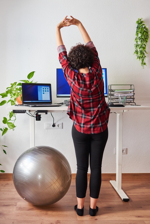 Woman stretches while working at an adjustable desk standing.