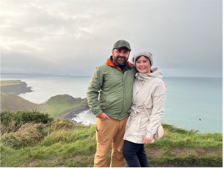 Two people standing near the edge of a cliff with the ocean in the background