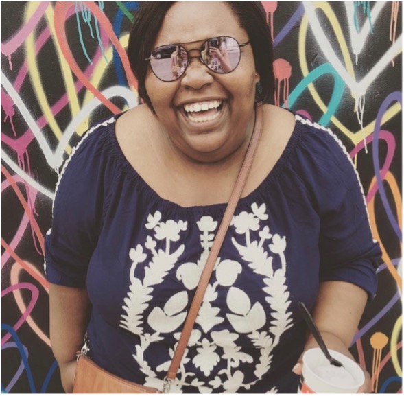 A person smiling and standing in front of a wall with graffiti art
