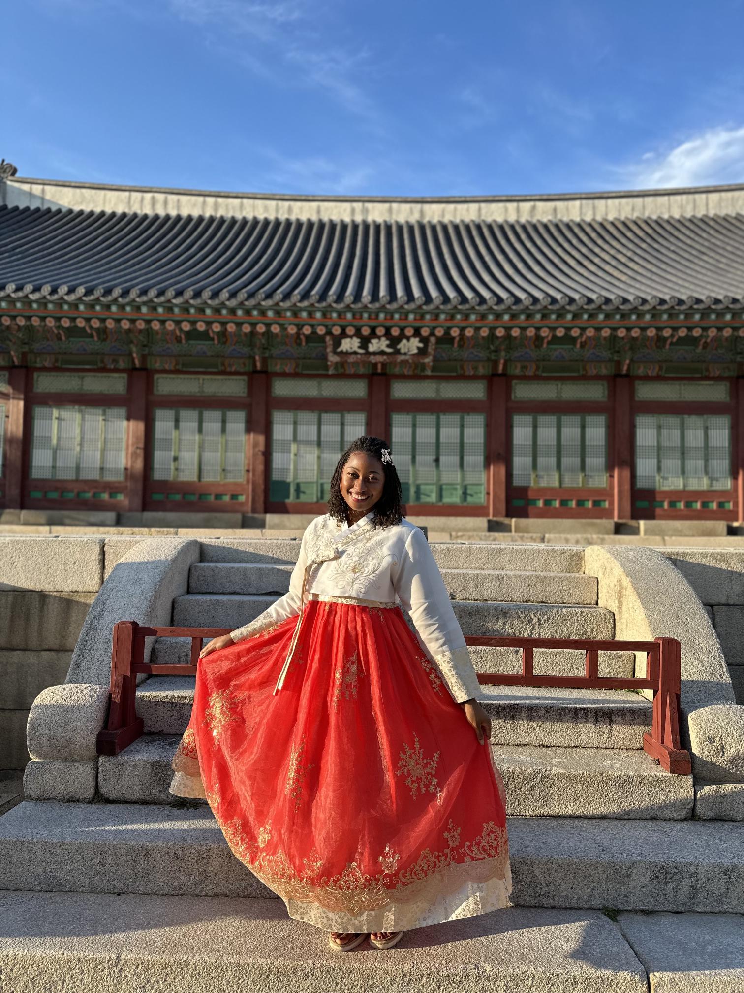A woman standing in front of step in a red and white dress. 