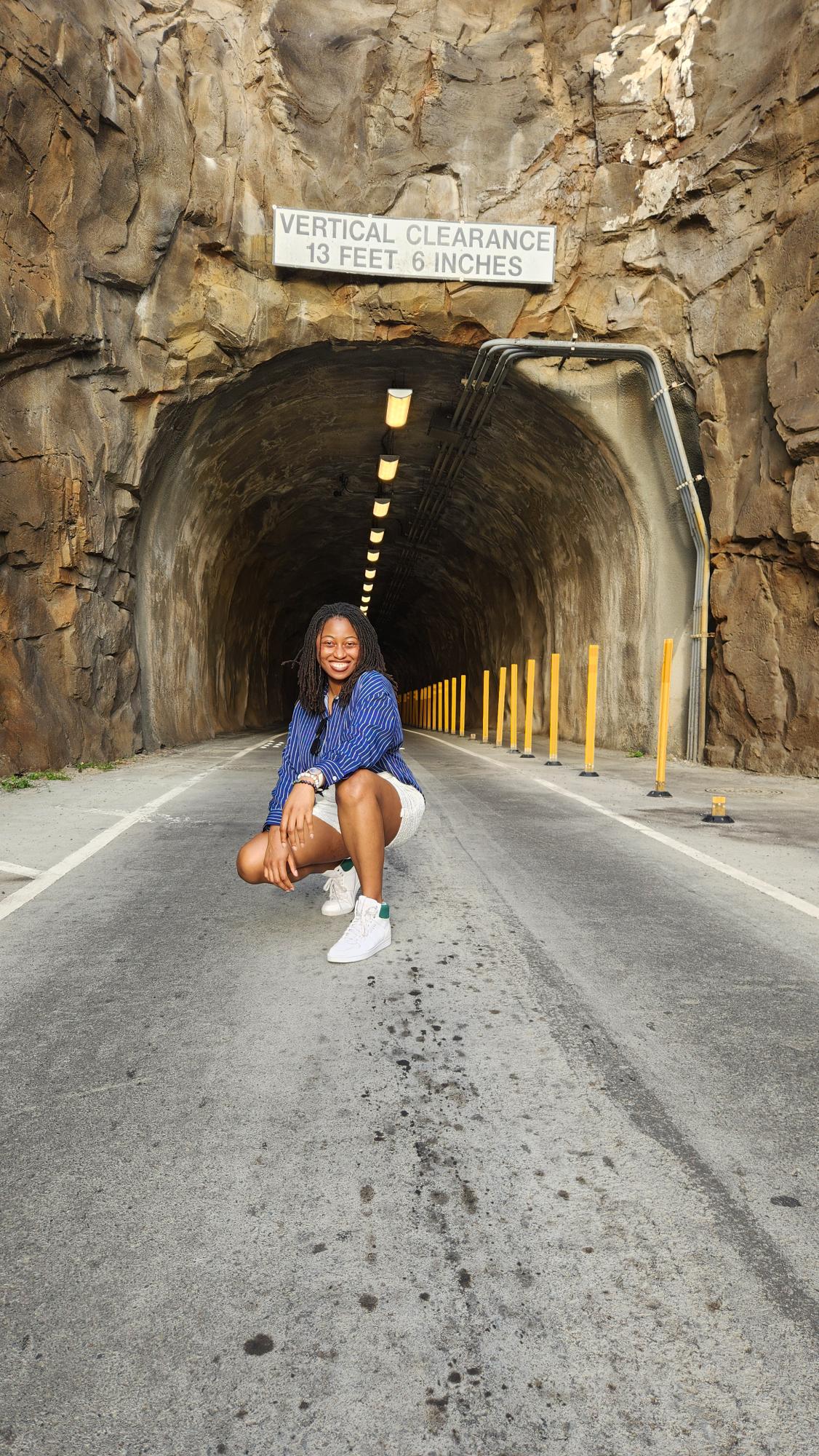 A woman crouching on a road at the opening of a long tunnel.