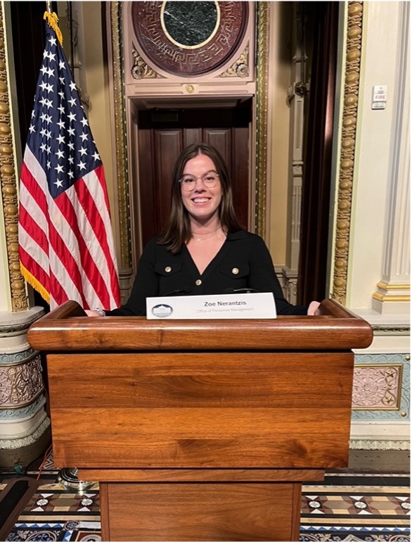 A woman standing at a podium with an American flag to the left of her.