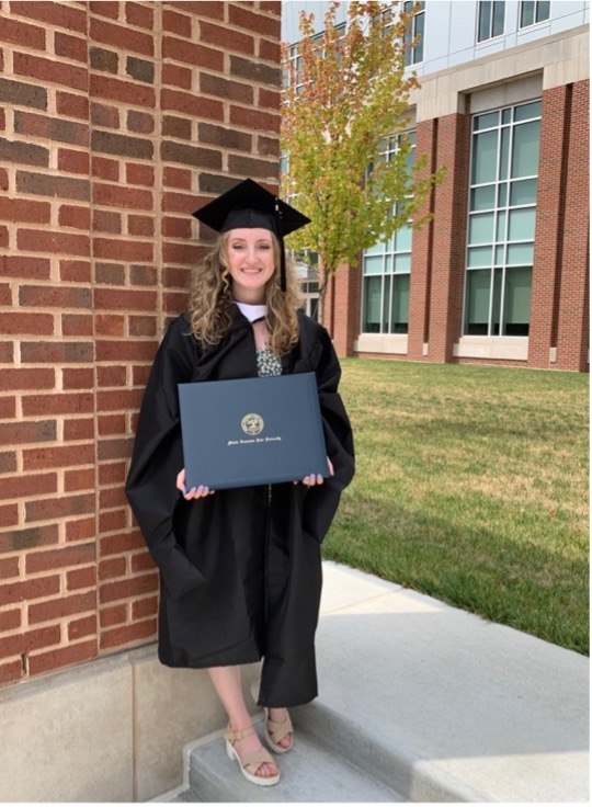 A person standing in graduation gowns holding a diploma.