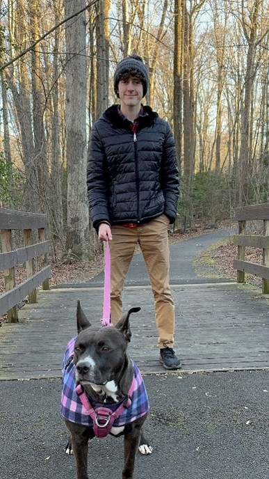A man standing holding a dog on a leash, standing on a small bridge.